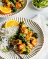 Close-up side angle of orange chicken and broccoli on a plate with rice. Fork set on plate.
