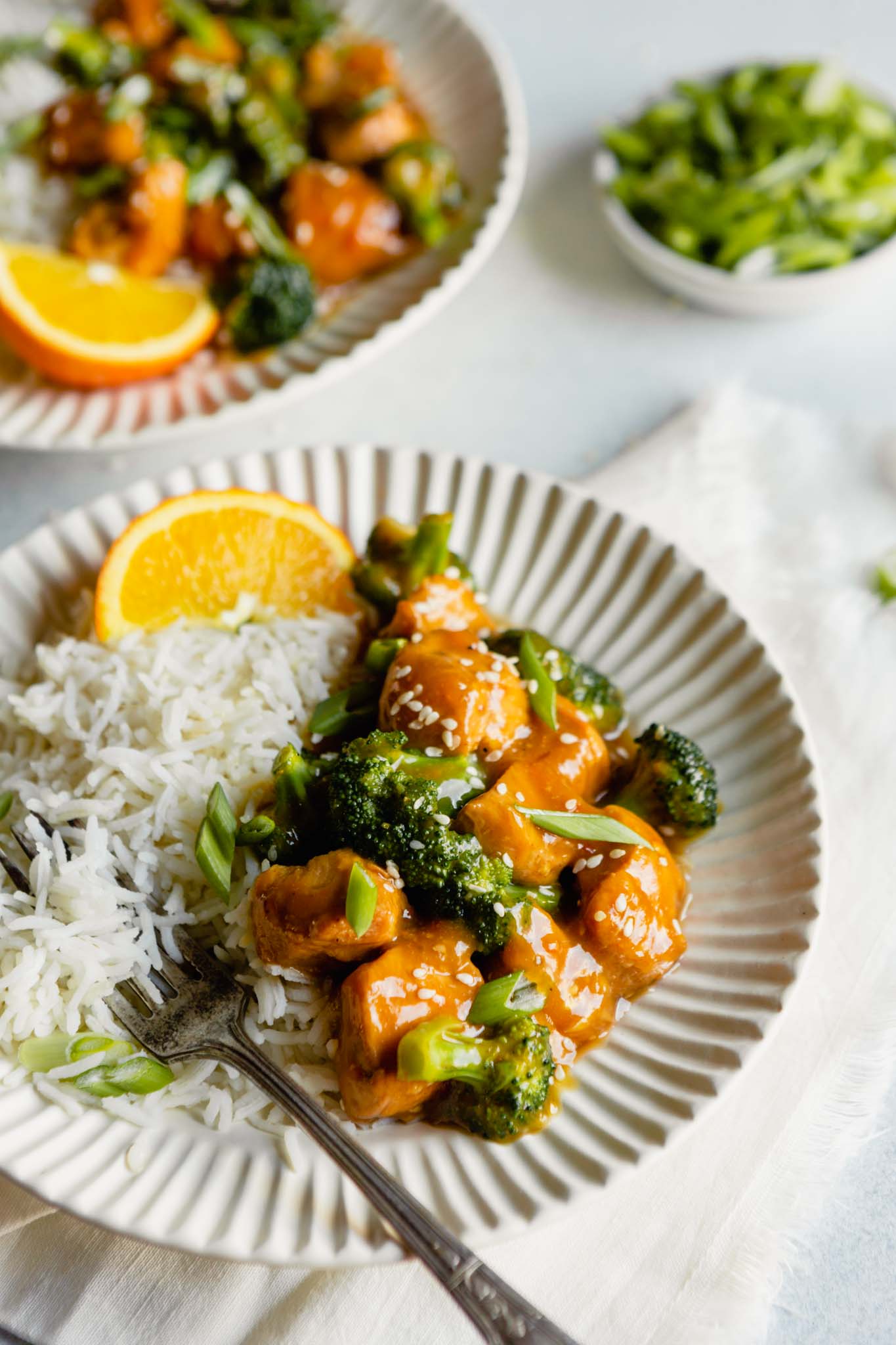 Close-up side angle of orange chicken and broccoli on a plate with rice. Fork set on plate. 