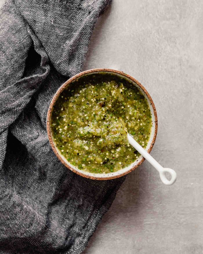 Overhead image of green salsa in a white speckled bowl set on a gray table with a dark napkin off to the side