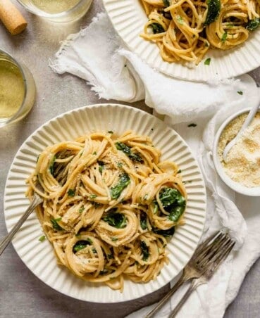 Overhead image of whole wheat pasta with spinach and Parmesan served in white bowls with wine and parmesan off to the side