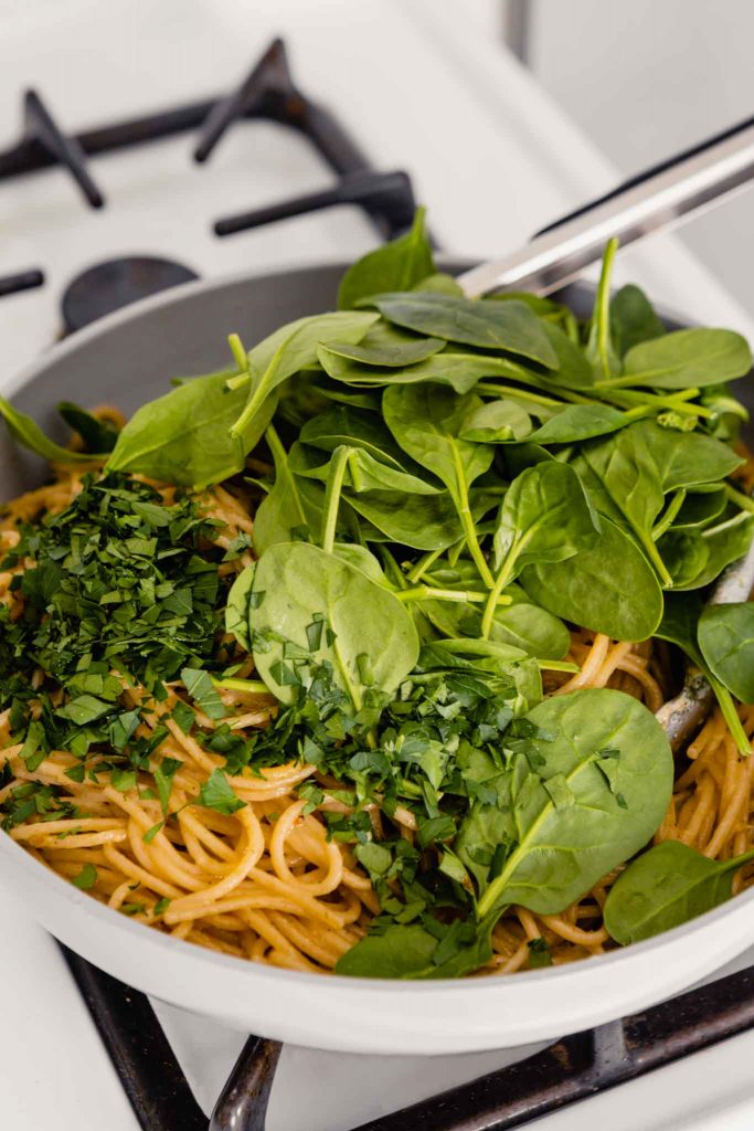 image of spinach and parsley on top of a bed of noodles in a gray skillet on the stove