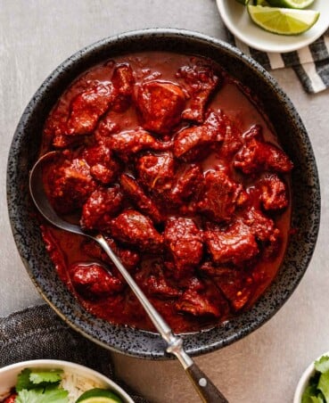 overhead image of deep red carne adovada in a dark gray bowl set on a gray table