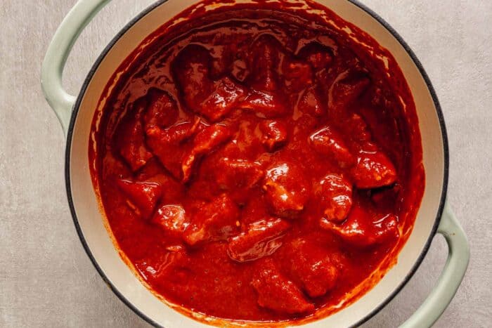 Overhead image of chunks of pork laying in a red chile sauce in a Dutch oven