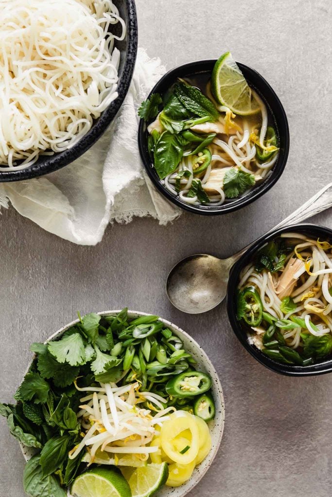 Overhead image of bowls of pho soup in a black bowl set on a gray table