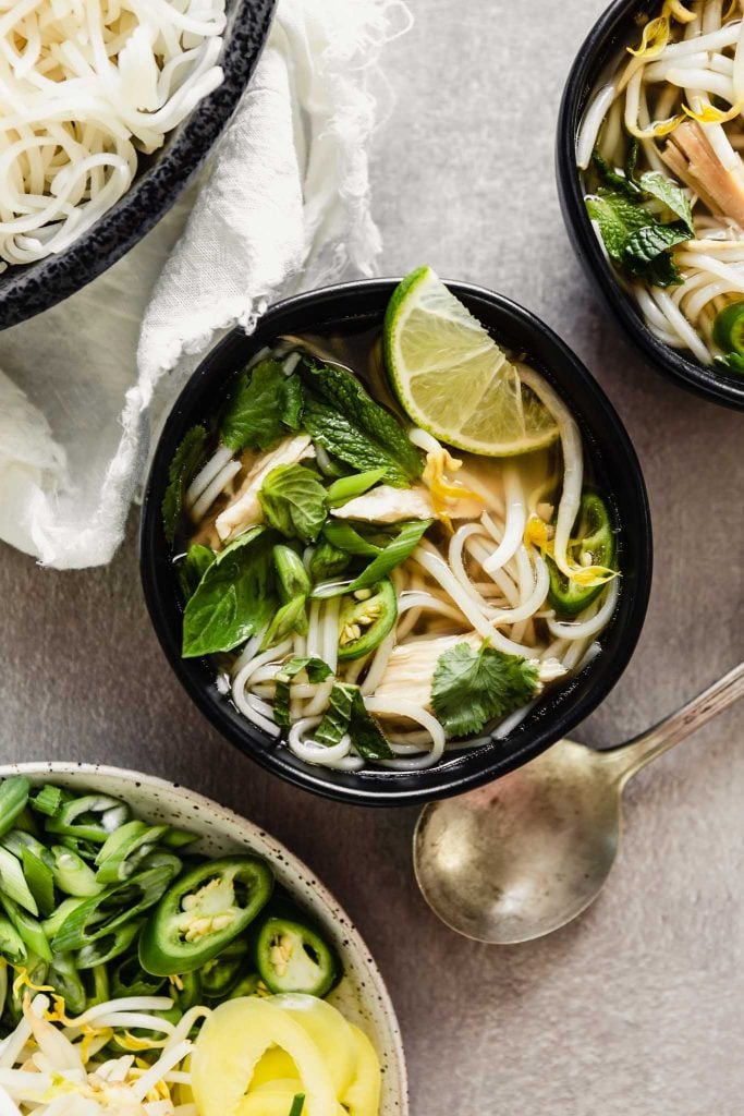 Overhead image of pho soup in a black bowl set on a gray table