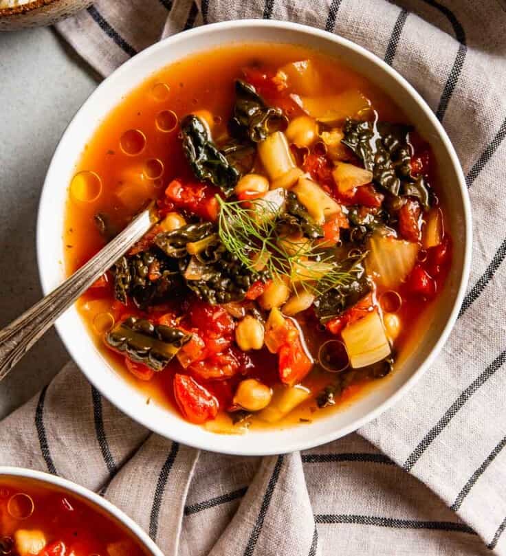 tomato and kale soup in a shallow white bowl with chickpeas and olive oil droplets