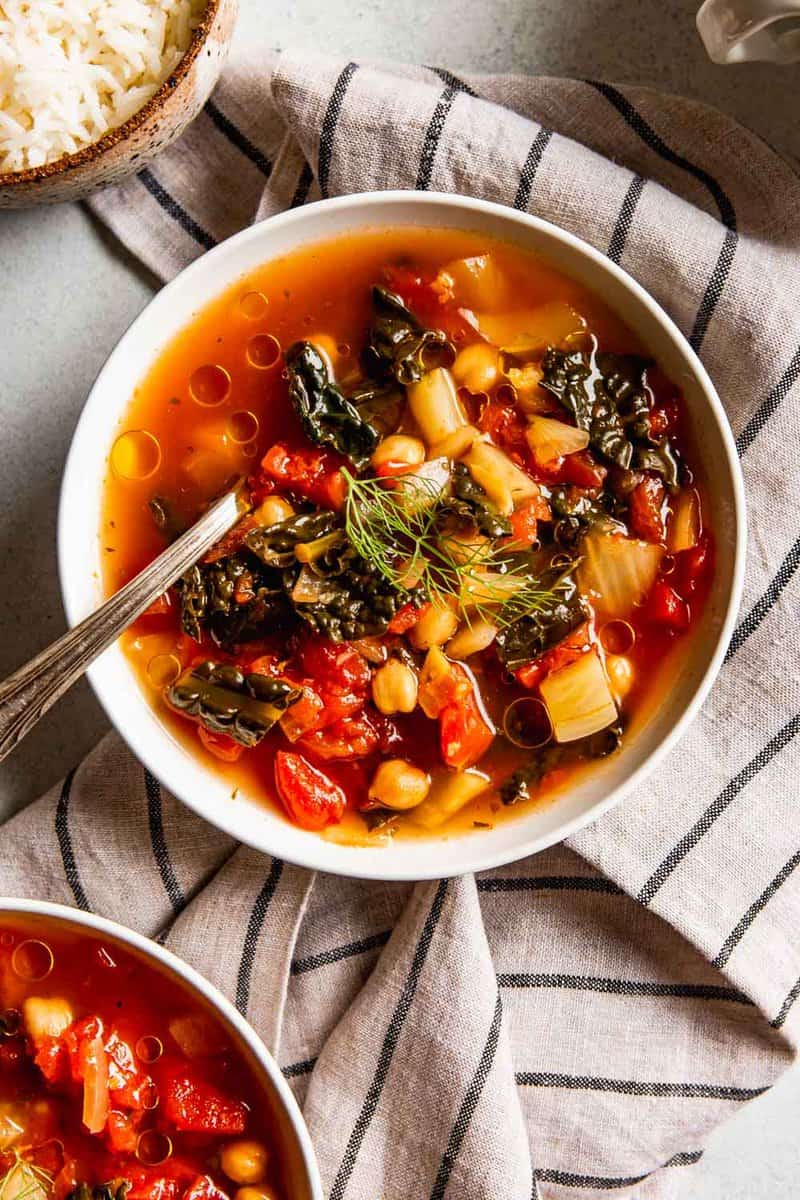 tomato and kale soup in a shallow white bowl with chickpeas and olive oil droplets
