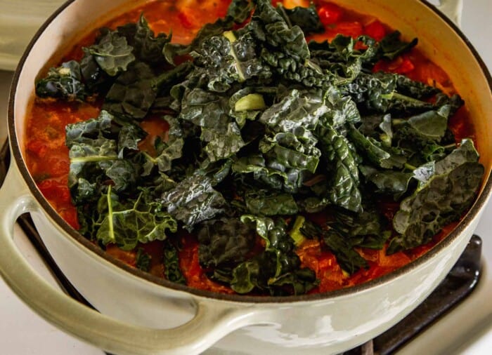 mounded kale in a Dutch oven filled with tomatoes and broth
