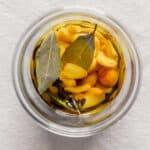 Overhead image of garlic cloves and bay leaves in a jar covered with oil