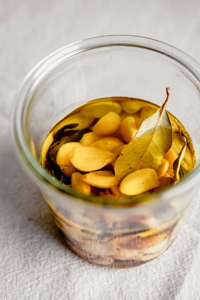 45-degree angle of garlic cloves and bay leaves in a jar covered with oil