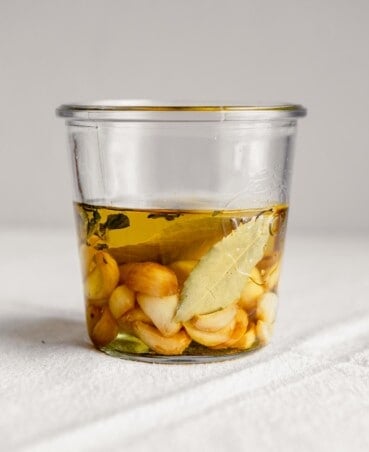 Side angle of garlic cloves and bay leaves in a jar covered with oil