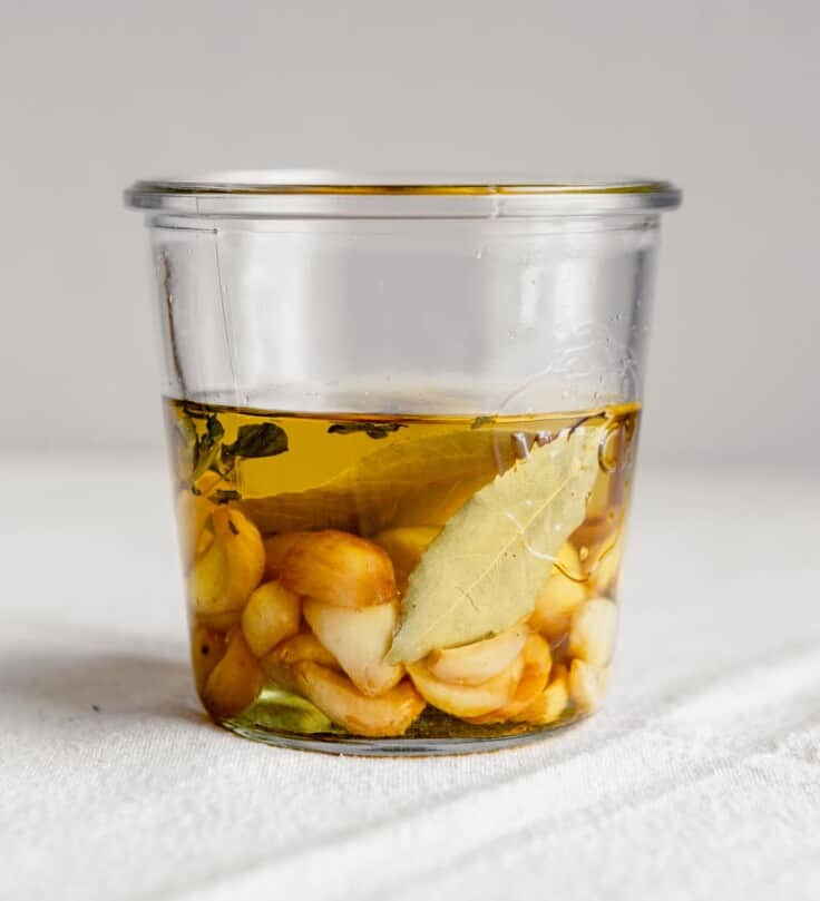 Side angle of garlic cloves and bay leaves in a jar covered with oil