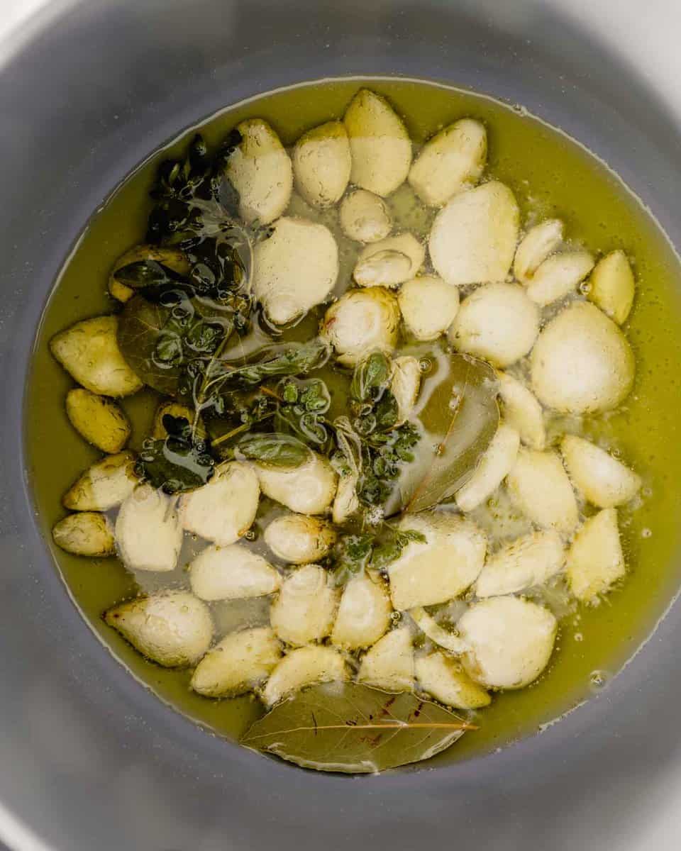 photo of garlic cloves in a saucepan with simmering oil and herbs