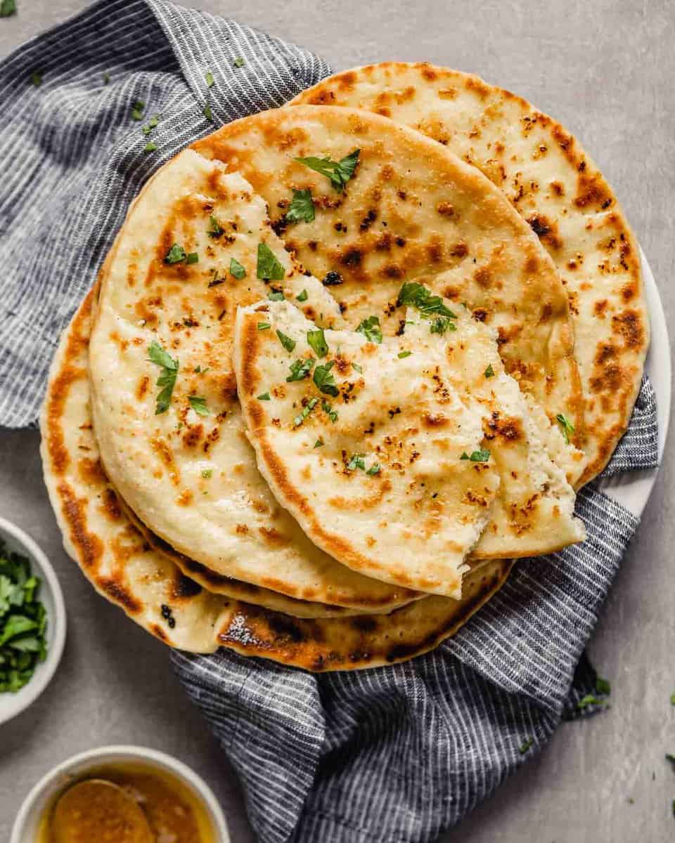 Homemade naan bread stacked on a blue napkin on a white plate sprinkled with parsley