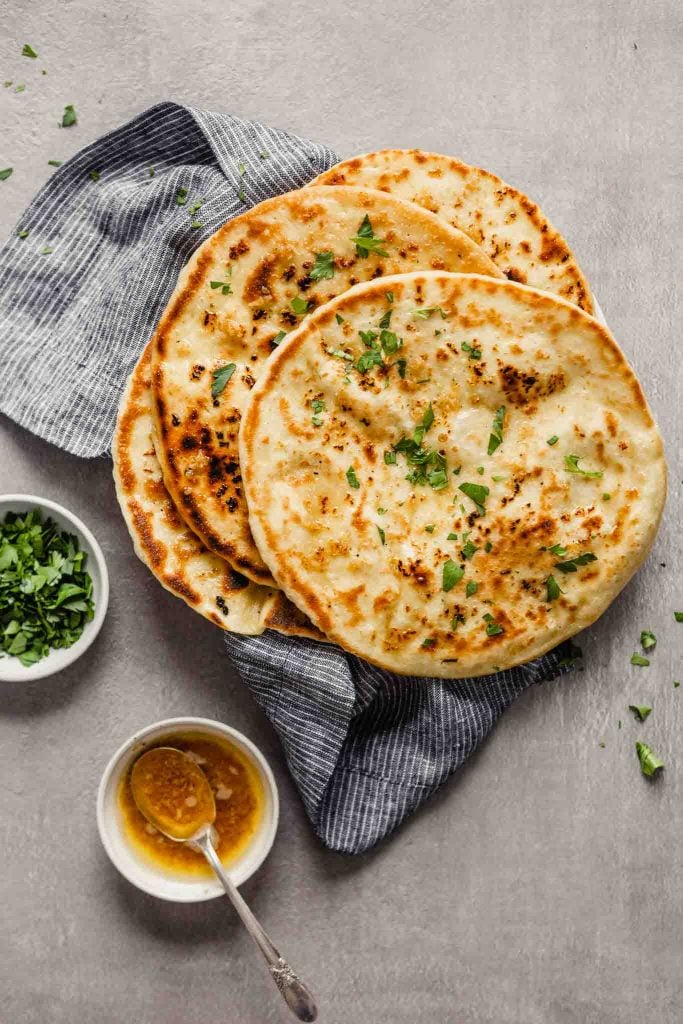 Homemade naan bread stacked on a blue napkin on a white plate sprinkled with parsley