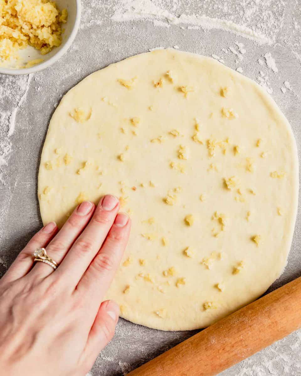 Overhead round of dough on a gray table topped with minced garlic