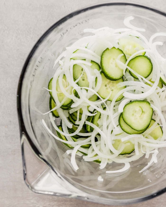 overhead image of thinly sliced cucumbers and onions in a glass bowl