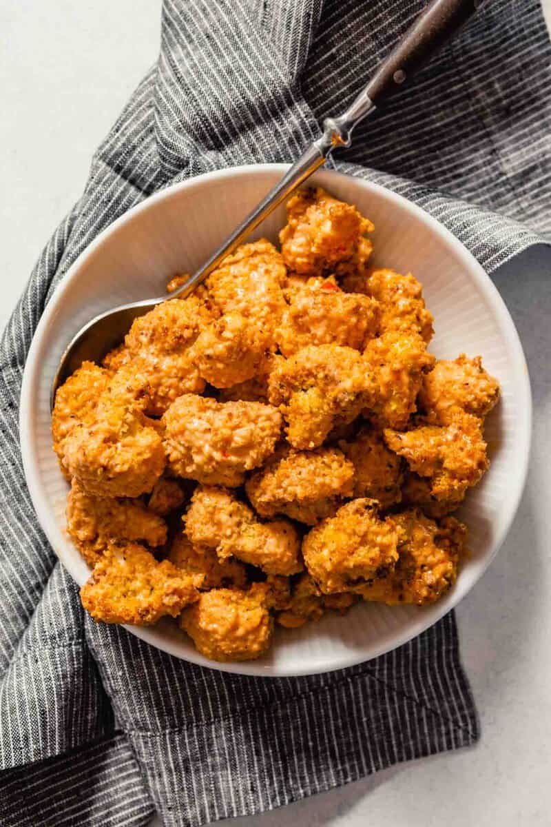 overhead image of breaded and baked cauliflower bites in a white bowl set on a dark napkin