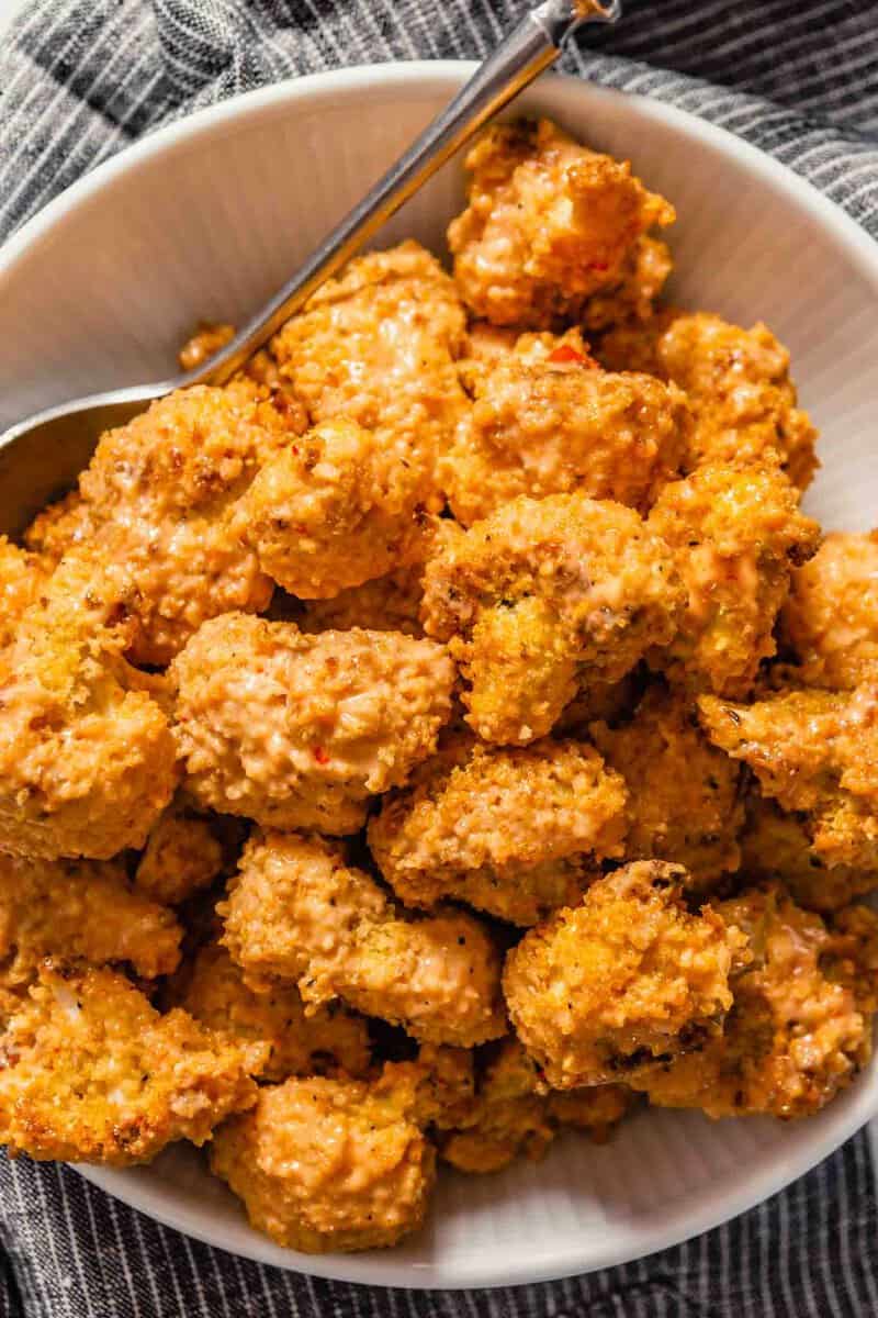 Close up overhead image of breaded and baked cauliflower bites in a white bowl set on a dark napkin