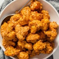 Close up overhead image of breaded and baked cauliflower bites in a white bowl set on a dark napkin