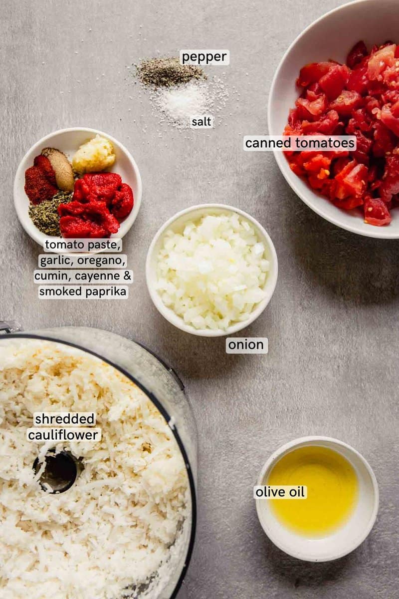 overhead image of ingredients (cauliflower, oil, onion, tomatoes, tomato paste, spices) laid out on a gray counter
