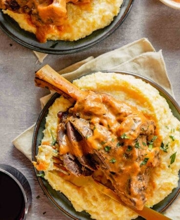 overhead angle of a sliced lamb shank covered with sauce set over a bed of polenta on blue plates