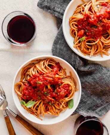 overhead image of spaghetti and red sauce in a white bowl set on a table with wine and parmesan