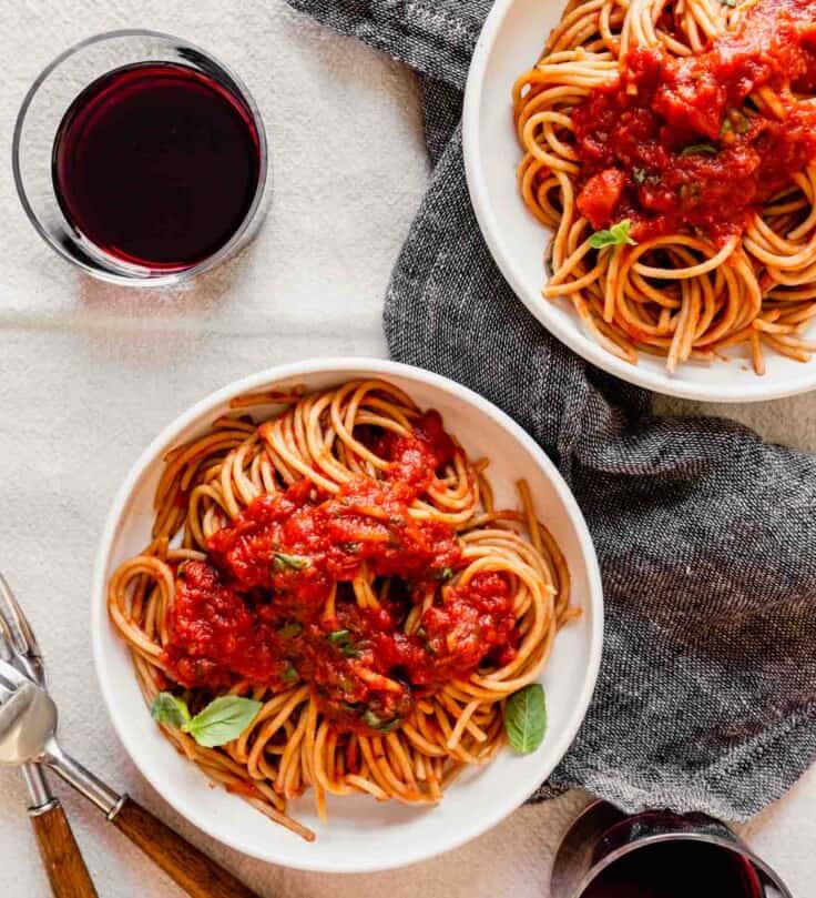 overhead image of spaghetti and red sauce in a white bowl set on a table with wine and parmesan