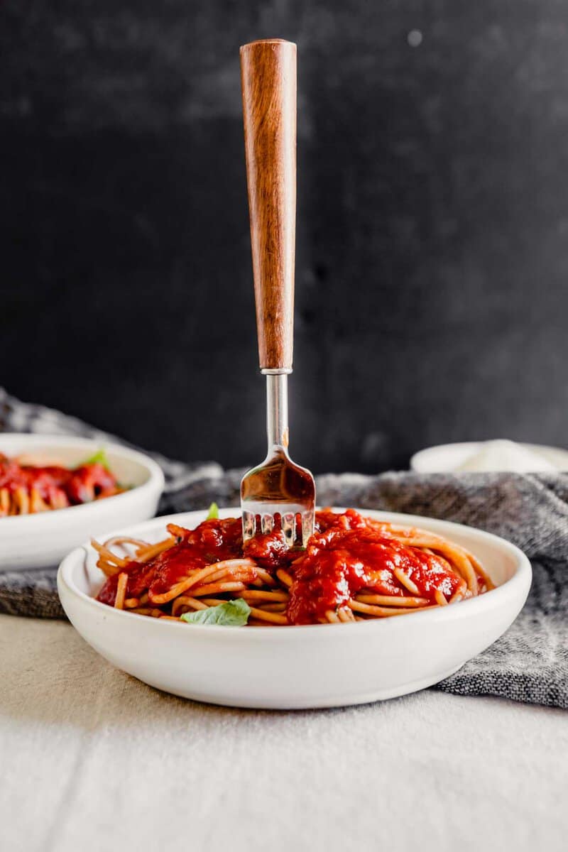 Side angle of a fork stuck straight up in a bowl full of spaghetti and sauce