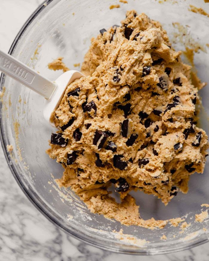overhead image of cookie dough with chocolate chunks in a clear glass bowl with a white spatula in it