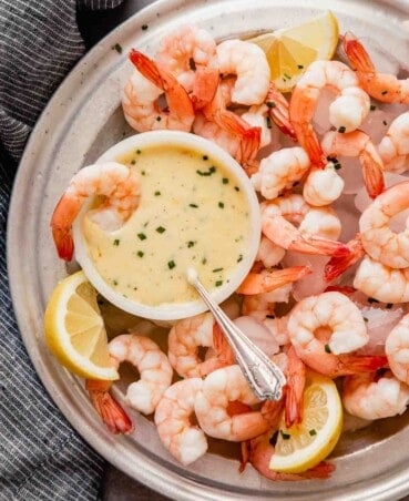 Overhead image of a metal plate filled with ice, shrimp, and a butter sauce in a white bowl