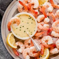 Overhead image of a metal plate filled with ice, shrimp, and a butter sauce in a white bowl