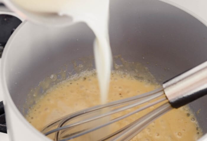 milk being added to creamy sauce in saucepan