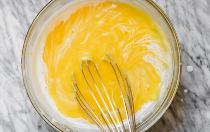lemon curd with a splash of cream in a glass bowl with a whisk