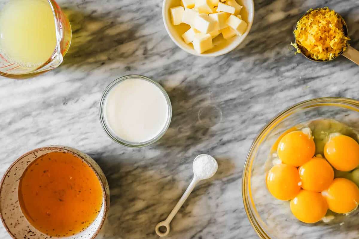 butter, cream, honey, eggs, lemon zest, and lemon juice set out on a counter