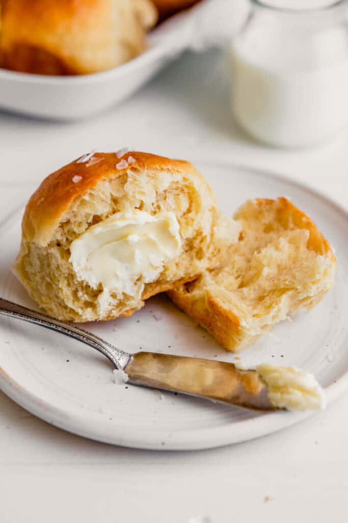 Side angle image of a milk roll topped with butter set on a plate