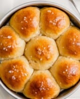 Overhead image of milk rolls in a round cake pan set on a white table