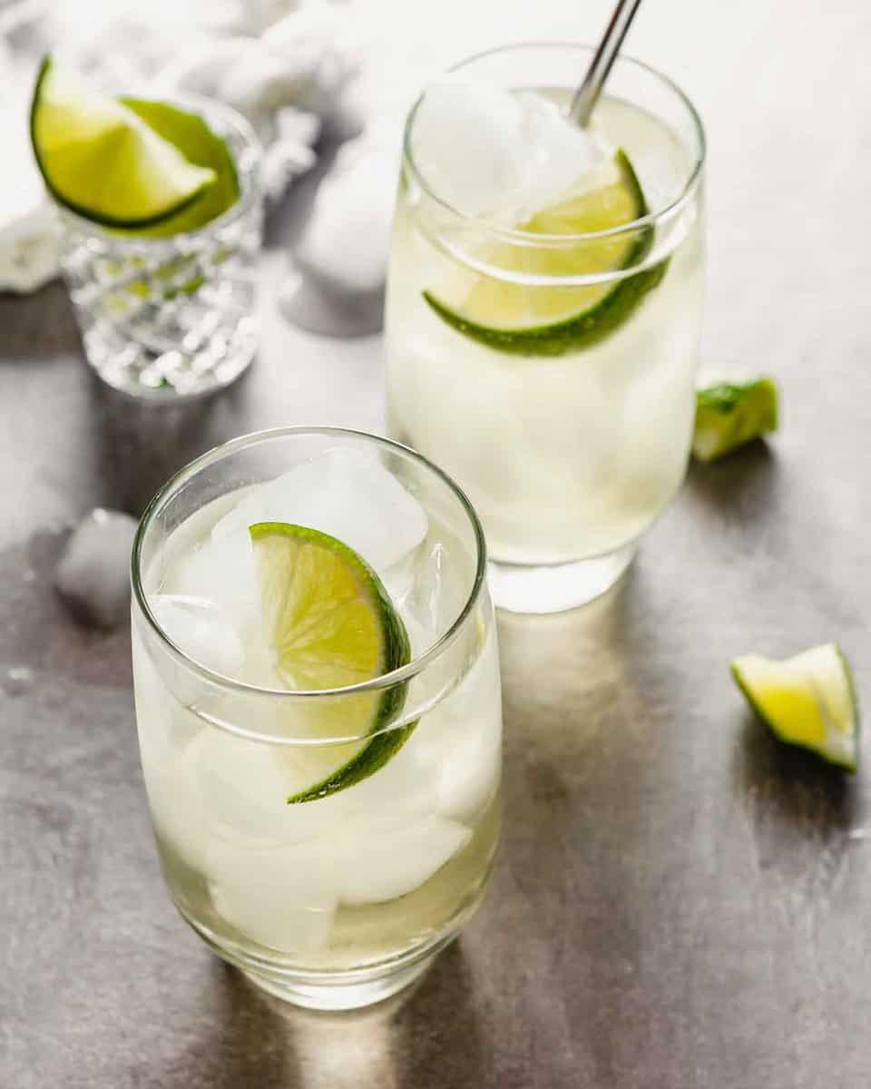 Side angled image of high ball glasses filled with a cocktail and a lime wedge.