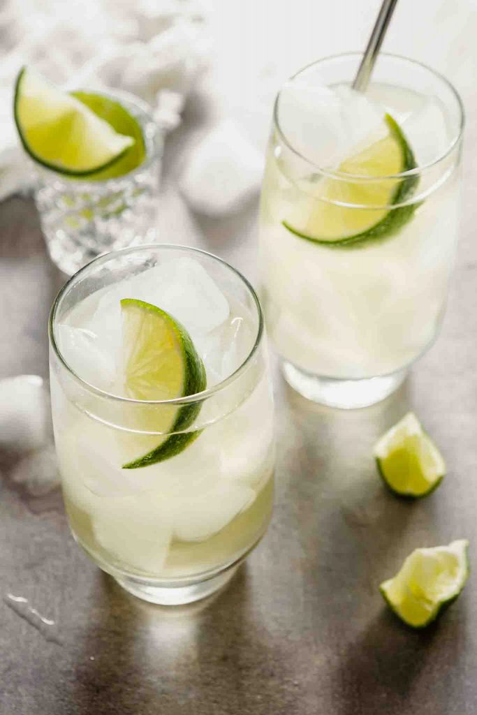 Side angled image of high ball glasses filled with a cocktail and a lime wedge.