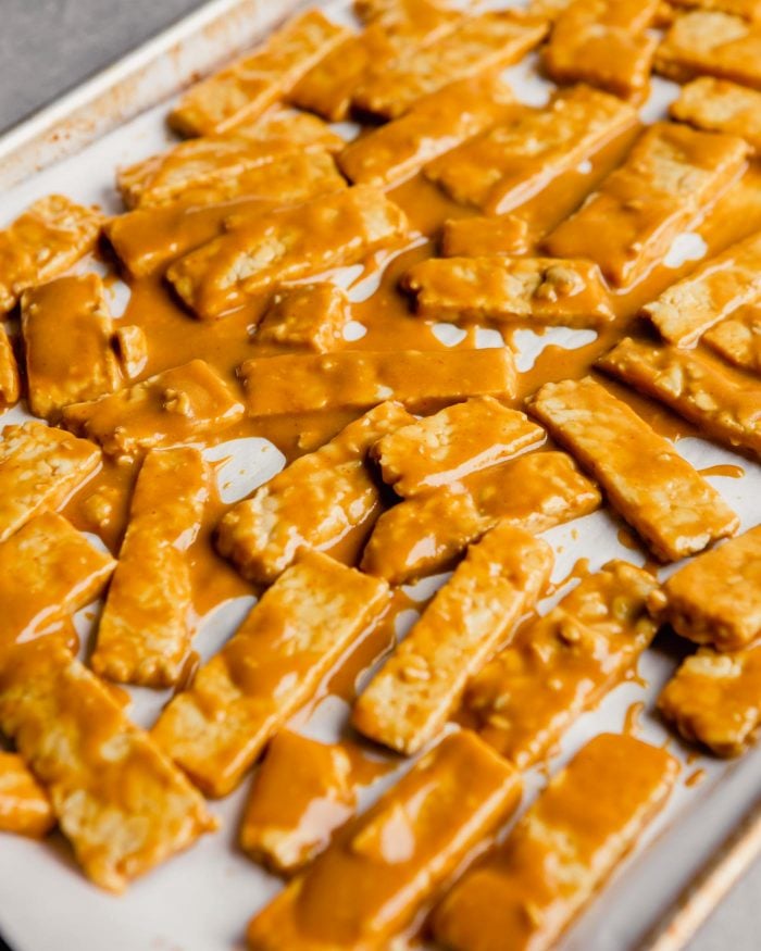 tempeh coated in bbq sauce arranged in a single layer on a parchment-lined baking sheet