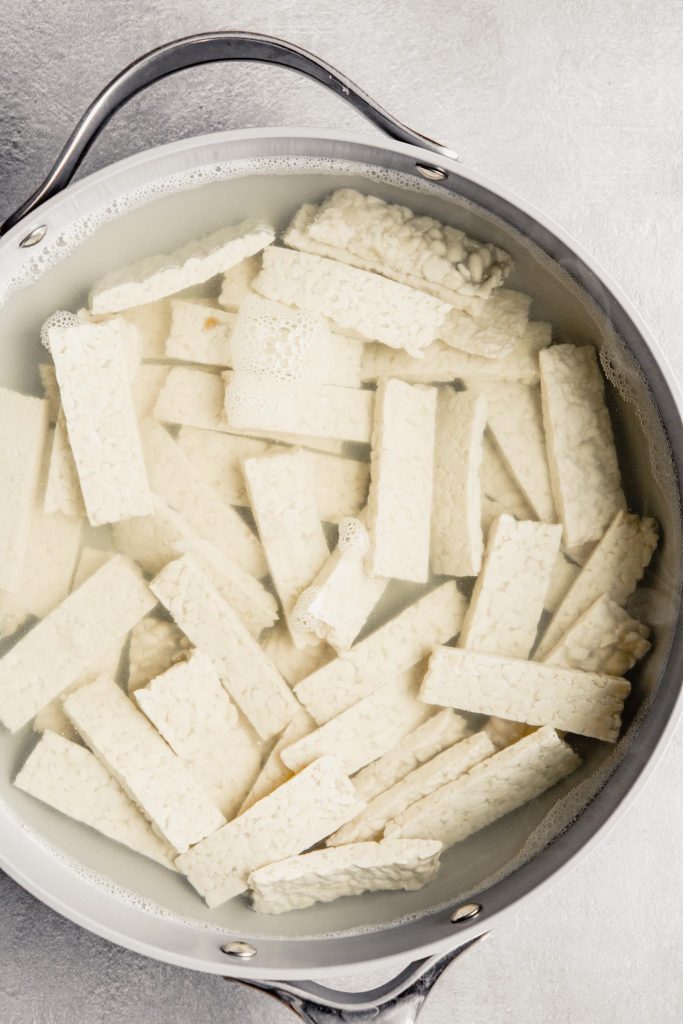 tempeh pieces submerged in water in a large skillet