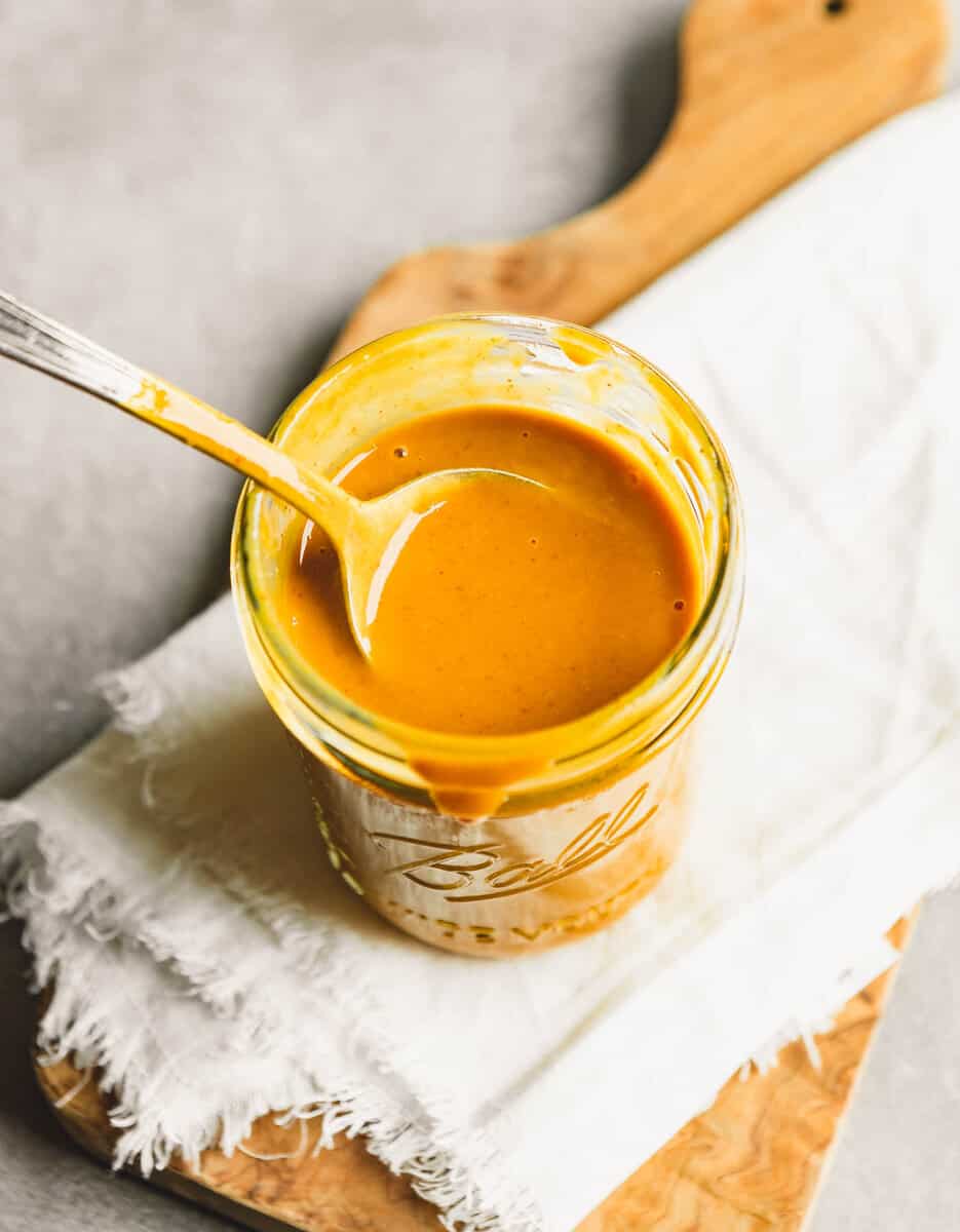yellow-orange sauce being spooned fro a glass jar