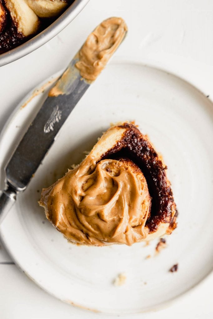 close up image of a frosted cinnamon roll on a white plate with a knife