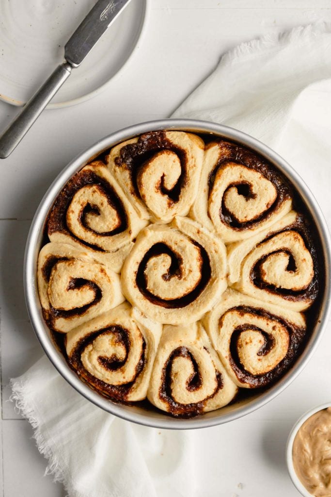 overhead image of baked cinnamon rolls in a round cake pan 
