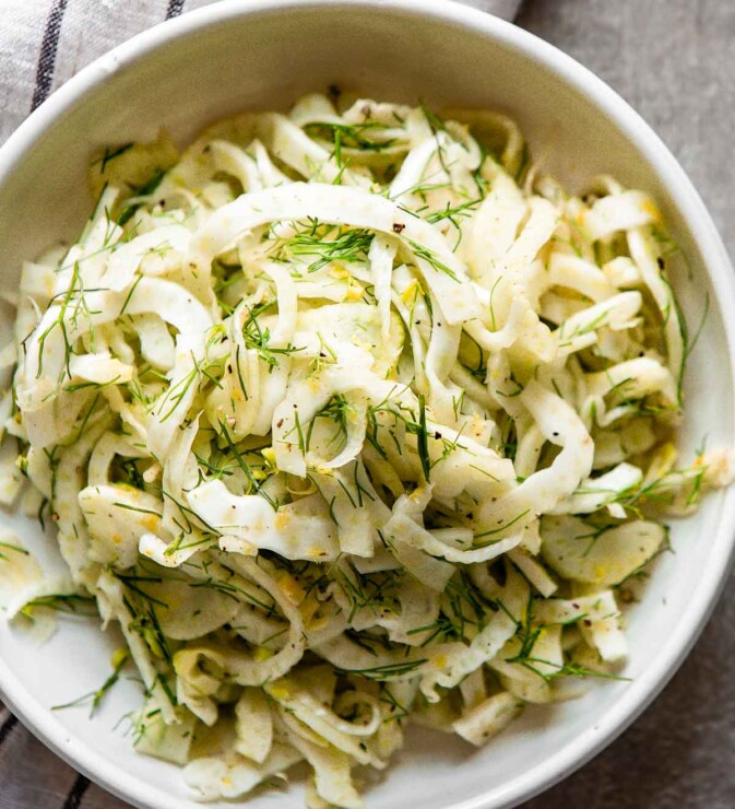 shaved fennel in a dish with lemon dest, fennel fronds and black pepper