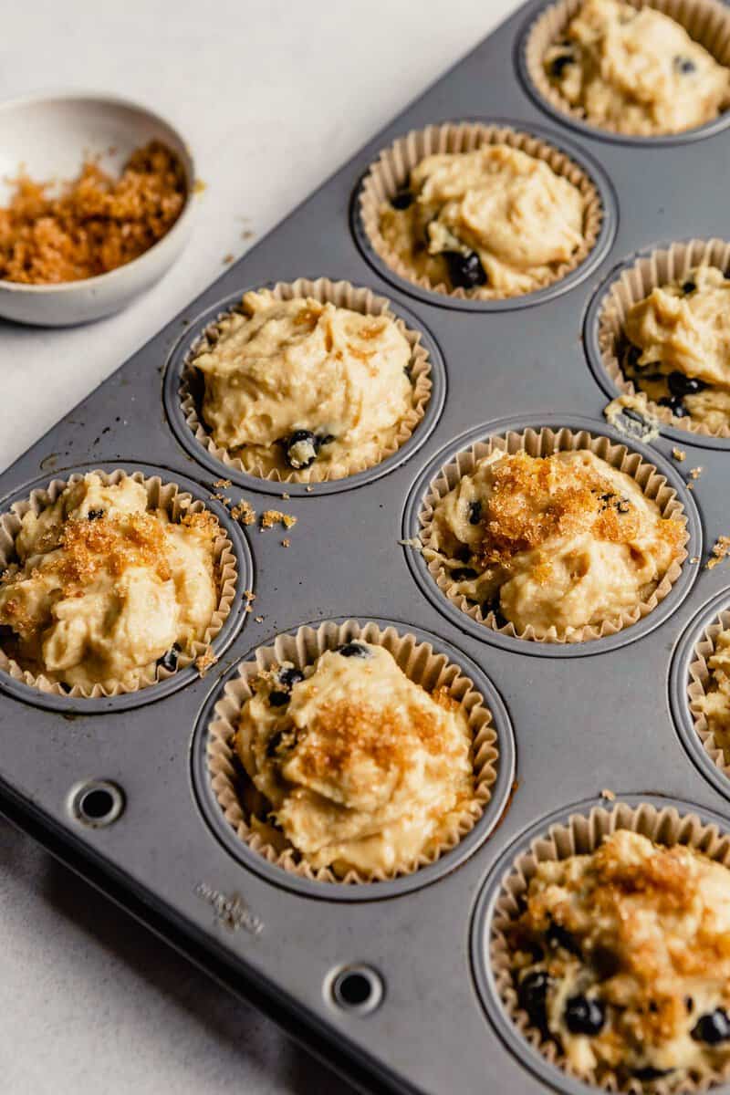 Healthy blueberry muffin batter in muffin tin topped with turbinado sugar.