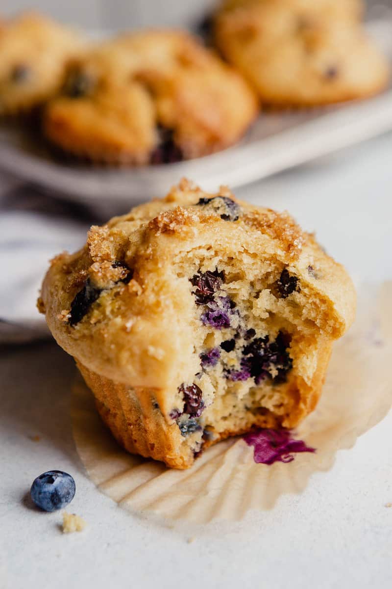 A blueberry muffin set on a countertop with a bite taken out of it.