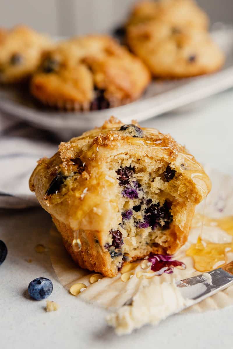 A blueberry muffin set on a countertop with a bite taken out of it and honey dripping down it.