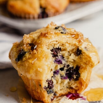 A blueberry muffin set on a countertop with a bite taken out of it and honey dripping down it.