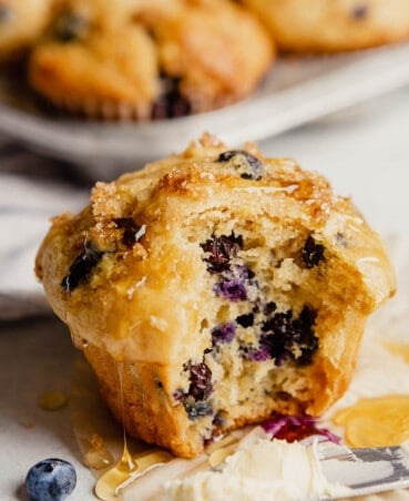 A blueberry muffin set on a countertop with a bite taken out of it and honey dripping down it.